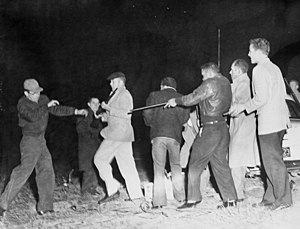 A black-and-white image of a group of Native Americans armed with firearms confronting a group of white people