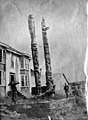 Women with parasol standing near Tlingit totem poles in front of Chief Kat-A-Shan's house, Fort Wrangell, Alaska, circa 1900 (AL+CA 6723).jpg