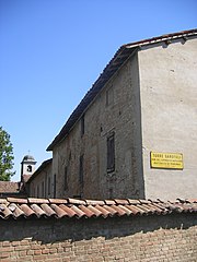 Small building with a courtyard surrounded by brick walls and a bell tower in the background.