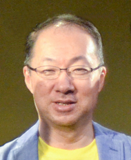 Portrait d'un homme brun de type asiatique, portant de petites lunettes.