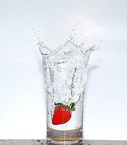 A strawberry falling into a glass of water