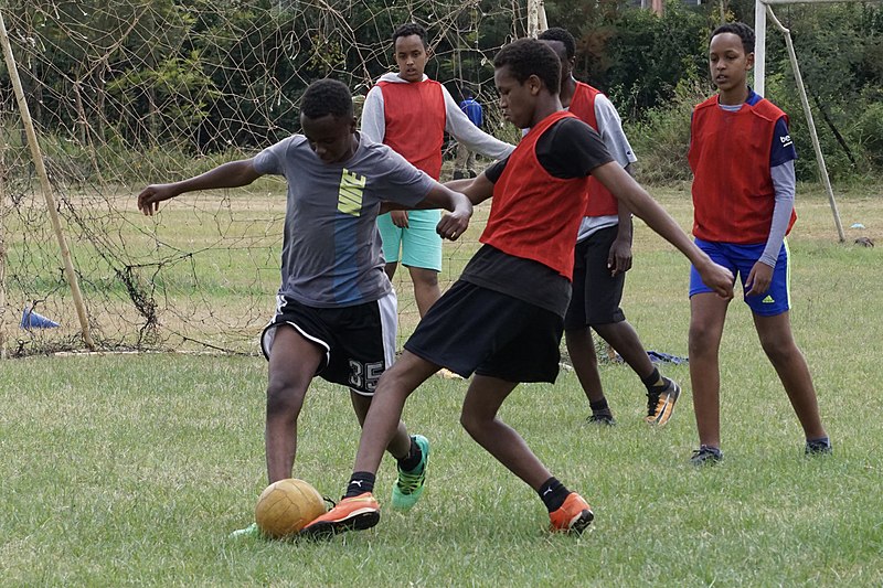 File:Teens battle for ball as teammates watch.jpg