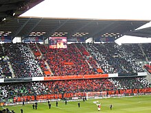 Foto, das eine Tribüne zeigt, mit Leuten, die weiße, rote und schwarze Fahnen schwenken.