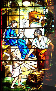 The Holy Family are outside their carpenter's shop where Joseph is working at his bench and Mary is sitting on the steps, spinning with a distaff. Joseph looks towards Mary as the child Jesus carries some wood resembling a cross.