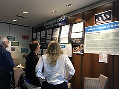 Participants in the first Day 1 Movement Strategy feedback session study the strategy timeline posted on a wall in the session room