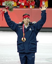 Аполо Оно, с поднятыми руками, с бронзовой медалью на шее.