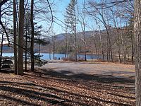 Pogled na jezero Douthat State Park s područja porinuća broda koji prikazuje plavo nebo, drveće, planine i vodu