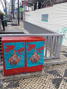 Photo presents the top of entrance of the metro station in Lisbon with street box covered by two colorful posters