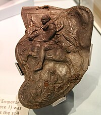 The "Emperor" cheekpiece (no. 1), depicting a Roman emperor being crowned by Victory while trampling a barbarian under his horse's hooves Hallaton helmet cheekpiece 1.jpg
