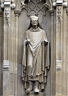 Statue en pierre d'un homme en robe située dans une niche.  La moitié supérieure de la tête de la statue est manquante.