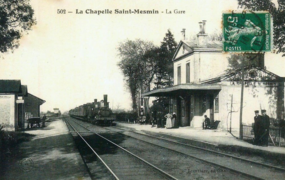Czarno-biała pocztówka przedstawiająca przybycie pociągu parowego przed starym dworcem.