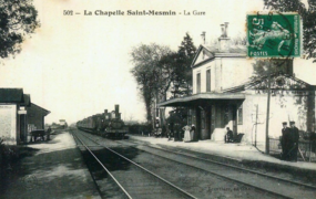 Schwarz-Weiß-Postkarte, die die Ankunft eines Dampfzuges vor dem alten Bahnhof darstellt.