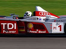 Photographie d'une voiture d'endurance grise et rouge, vue en gros plan, de profil.