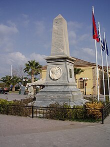 Farbfoto: ein Denkmal vom Typ eines grauen Steinobelisken und Flaggen