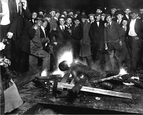 A group of white men pose for a 1919 photograph as they stand over the body of the Black lynching victim Will Brown before they decide to mutilate and