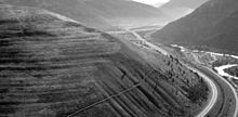 Wave-cut strandlines cut into the slope at left in photo. These cuts record former high-water lines, or shorelines. Gullies above the highway are the result of modern-day erosion. (NPS Photo) Orillas fosiles del lago Missoula.jpg