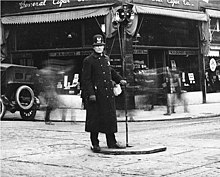 A Seattle Police Department officer directing traffic in downtown Seattle, 1922. Some early intersections featured concrete islands for traffic lights and traffic officers. Policeman, probably directing traffic, Seattle, Washington, March 7, 1922 (LEE 123).jpeg