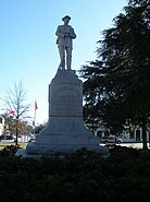 The statue of a Confederate soldier stands in the town square park. The pedestal reads: "Erected by The Daughters of the Confederacy to the Confederate Soldiers of Macon County".