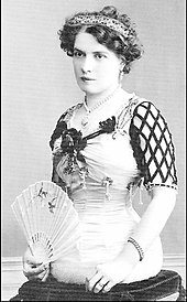 Antonia Matt um 1900: eine elegant gekleidete Dame mit eng geschnürter Taille und einem Fächer sitzt auf einem Kissen. Man sieht, dass sie keine Beine hat