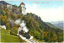 Schloss und Burgruine auf einer kolorierten Ansichtskarte aus dem Jahr 1909. Im Vordergrund ein Zug der Pyhrnbahn