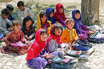 Schoolchildren sitting on the ground outside and smiling during a lesson