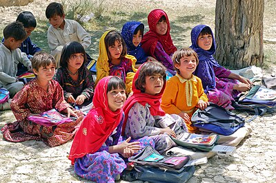 Schoolchildren sitting on the ground outside and smiling during a lesson