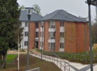 A large, three storey brick building with a path leading up to the entrance and some trees in the foreground.