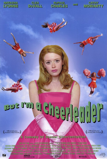 A half-length portrait of a young woman with long hair, wearing a bright pink formal dress and satin gloves. At a distance over her head five cheerleaders in orange outfits perform, flying through the sky. Across the portrait reads, "But I'm a Cheerleader", and below, in smaller letters, "A Comedy of Sexual Disorientation".