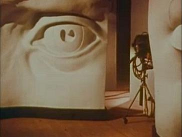 Screenshot from the opening credits of Gateways to the Mind (1958) showing part of William Kuehl's stage design. A camera is being rolled between giant sculptures of a human eye and a human mouth, which are props on a large and active soundstage.