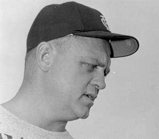 Neck-up black-and-white photograph of Holovak in profile wearing a dark baseball cap