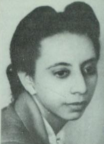 A Black woman with light skin, dark hair dressed back from her face, wearing a jacket and blouse