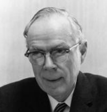 An older man with glasses, wearing a white shirt, with a darker coat and tie.