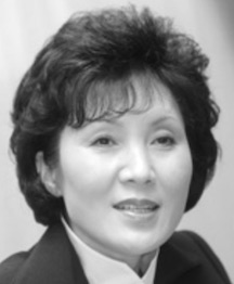Eine koreanische Frau mit kurzen dunklen Haaren, bauschig und gefiedert; Sie trägt einen dunklen Anzug und eine weiße Bluse oder ein weißes Hemd.