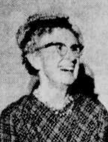 A smiling older white woman wearing glasses and a plaid dress