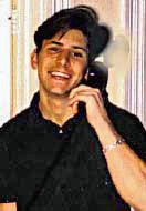 Молодой кавказский мужчина с темными волосами, в темной рубашке с воротником и расстегнутой верхней пуговицей, улыбается и прижимает к левому уху телефонную трубку.  За ним полосатый фон;  в правом верхнем углу его головы есть пикселированная область.