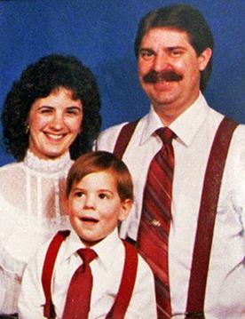Rodina s úsměvem do kamery na modrém pozadí.  Vlevo je tmavovlasá žena v bílé blůze s vysokým límcem a zuby se jí ukazují v úsměvu.  Uprostřed, dole, je mladý chlapec v bílé košili s červenými podvazky a kravatou, s otevřenými ústy.  Vpravo nahoře je muž podobně oblečený, s hnědými vlasy a knírem, pod kterým se usmívá se zavřenými rty.