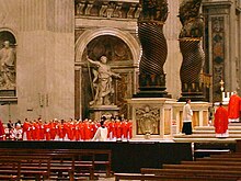 I cardinali, tutti in abiti rosso vivo, sono raggruppati vicino al baldacchino.