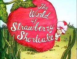 Sześcioletnia dziewczynka, ubrana w fartuszek i różową czapkę przeciwpyłową na włosach, spogląda na prawo od gigantycznej truskawki.  Na truskawce napis „Świat Truskawkowego Ciastka” jest napisany kursywą.