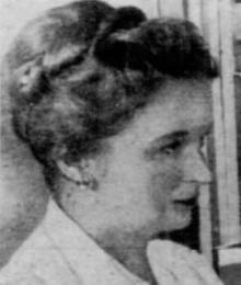 A white woman with hair in a top bun, wearing a labcoat, in profile