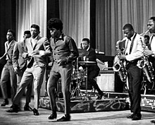 The Famous Flames (de gauche à droite : Bobby Bennett, Lloyd Stallworth, Bobby Byrd et James Brown) se produisant à l'Apollo Theatre de New York, 1964. Le groupe de Brown est à droite.