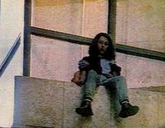 A young woman standing on the ledge of a building, looking down.