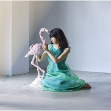 Ein Bild des Aufnahmekünstlers Haruka Chisuga, der sich neben eine Flamingoskulptur setzt.