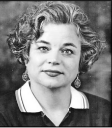 Portrait of a woman with short hair, large earrings, and wearing a dark top with a white collar