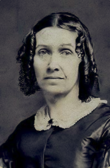 B&W portrait photo of a woman with dark hair in ringlets, wearing a dark blouse with a white collar.
