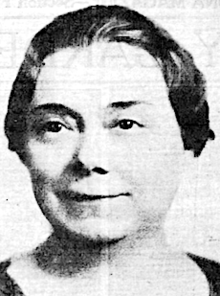 A middle-aged white woman with dark hair brushed back from face and up from neck