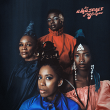 Four Black women with various hairstyles and bright clothes looking towards the camera in front of a dark backdrop