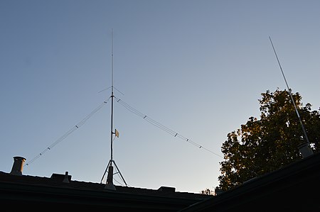 Typical amateur radio inverted vee installed on roof. This multiband antenna allows transmissions on the 40/20/15/10 meter bands. Center point is held up with masting and ends are secured to roof. Two VHF verticals are also shown. PIcture of ham radio inverted vee antenna.jpg