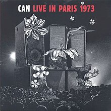 A black and white illustration of a stack of six broken speakers with flowers growing out of some of them; across the top is the following text on a black background: "CAN" in white, followed by "LIVE IN PARIS 1973" in red