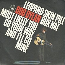 Single-Cover mit den Songtiteln in großem Text und Bob Dylan im Stehen, der eine Akustikgitarre hält