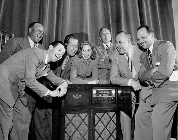 The cast of The Jack Benny Program, from left to right: Eddie "Rochester" Anderson, Dennis Day, Phil Harris, Mary Livingstone, Jack Benny, Don Wilson, and Mel Blanc